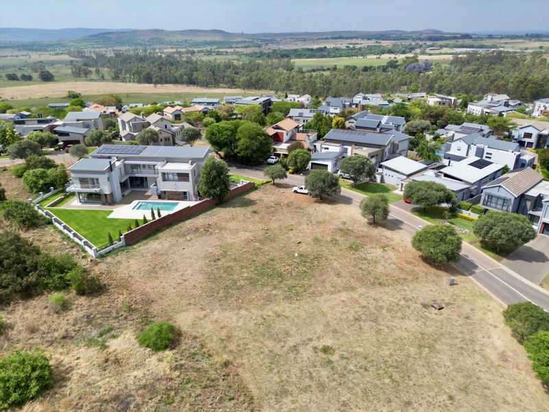 Aerial view of a vacant residential plot situated within a developed estate, offering clear potential for new construction in a scenic landscape.