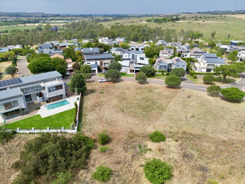 An aerial view of a vacant residential plot situated within a developed estate, surrounded by established homes and natural landscape.