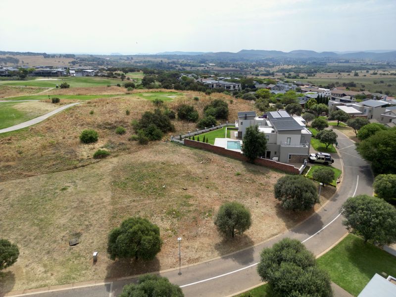 Aerial view of a vacant residential plot situated in a developed estate, featuring surrounding greenery and established road infrastructure.
