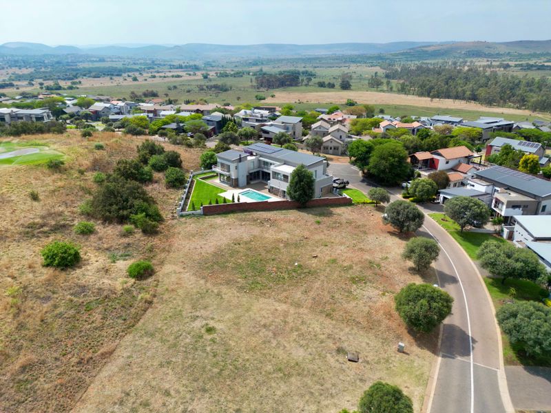 Aerial view of a residential property featuring a swimming pool, solar panels, and landscaped grounds within a secure estate setting.