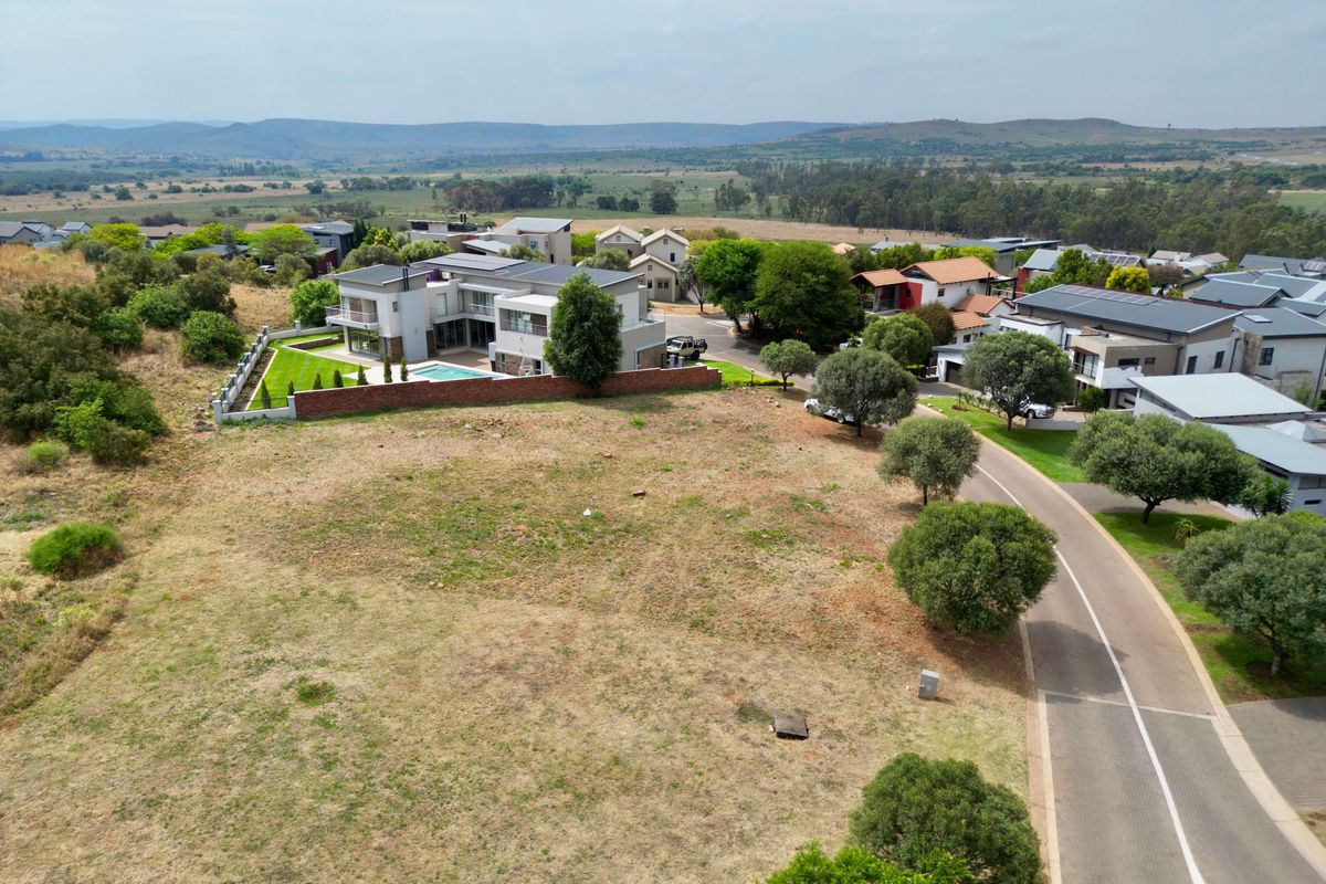 An aerial view of a vacant residential plot situated within a developed estate, featuring surrounding greenery and established neighborhood infrastructure.