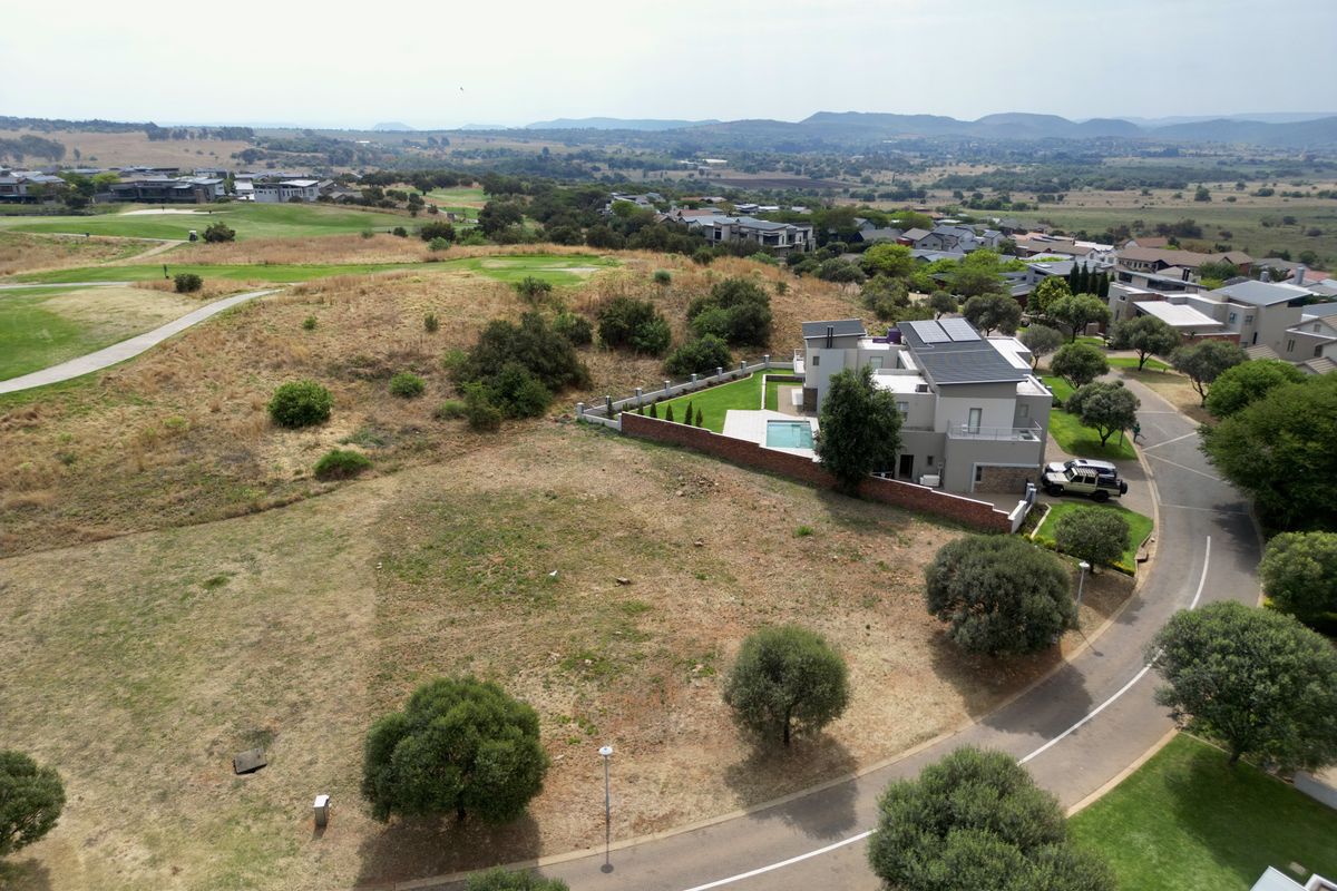 Aerial view of a vacant residential plot situated in a developed estate, featuring surrounding greenery and established road infrastructure.