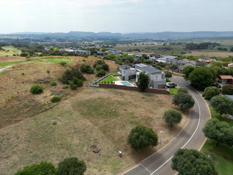 An aerial view of a residential property featuring a landscaped garden, swimming pool, and boundary wall, situated in a scenic estate setting.