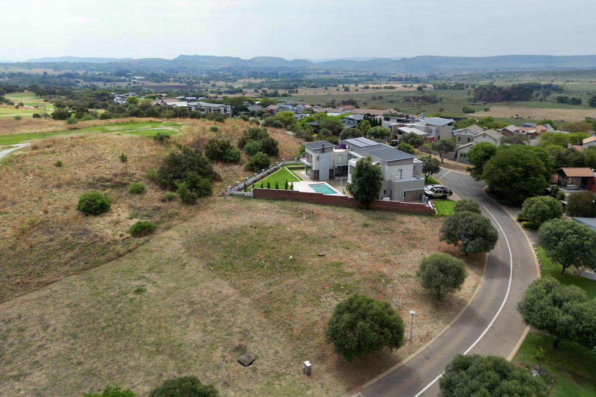 An aerial view of a residential property featuring a landscaped garden, swimming pool, and boundary wall, situated in a scenic estate setting.