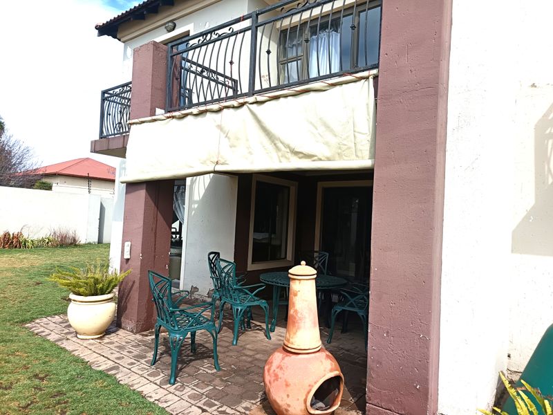 Covered ground-floor patio featuring paved flooring, masonry columns, and an overhead balcony with wrought iron railings and a retractable awning.