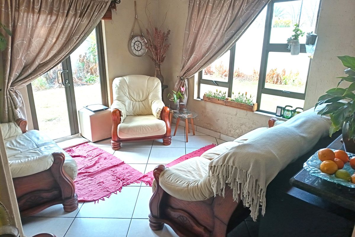 A living room featuring tiled flooring, large windows with aluminium frames, and a sliding door providing access to the garden area.