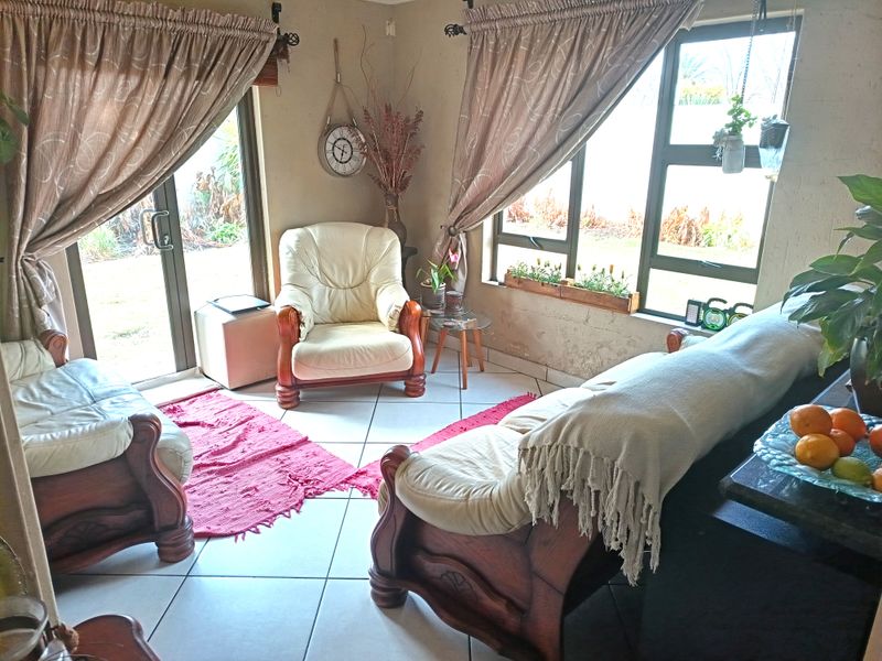 A living room featuring tiled flooring, large windows with aluminium frames, and a sliding door providing access to the garden area.