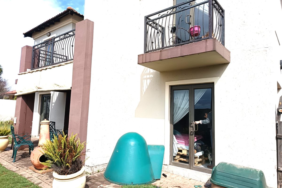 Rear elevation of a two-story house featuring a paved patio area, sliding glass doors, and upper-level balconies with wrought iron railings.