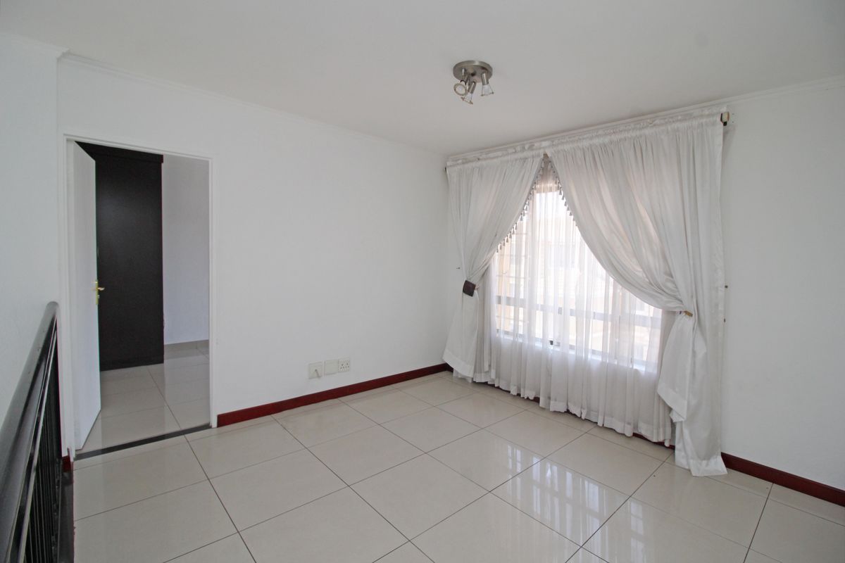 A bright, empty living area featuring neutral tiled flooring, white walls, and a large window with curtain fixtures.