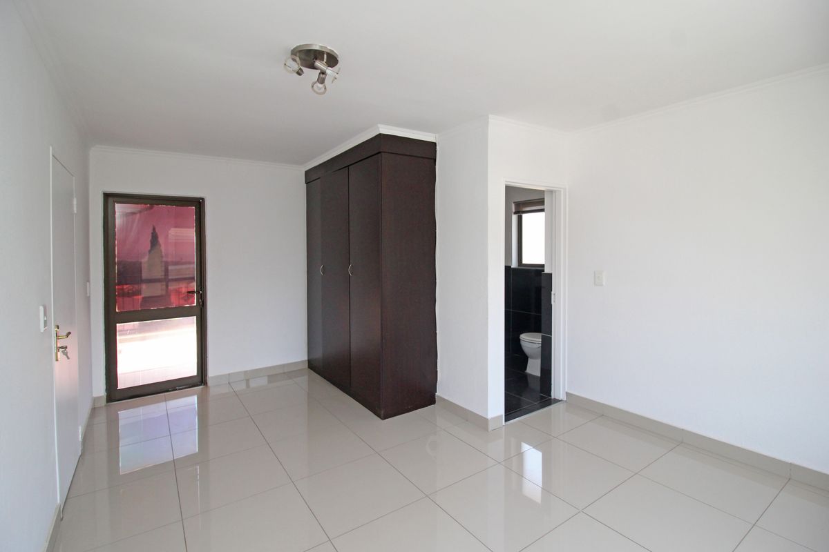 A bright bedroom featuring neutral floor tiles, a built-in dark wood wardrobe, and direct access to an en-suite bathroom.