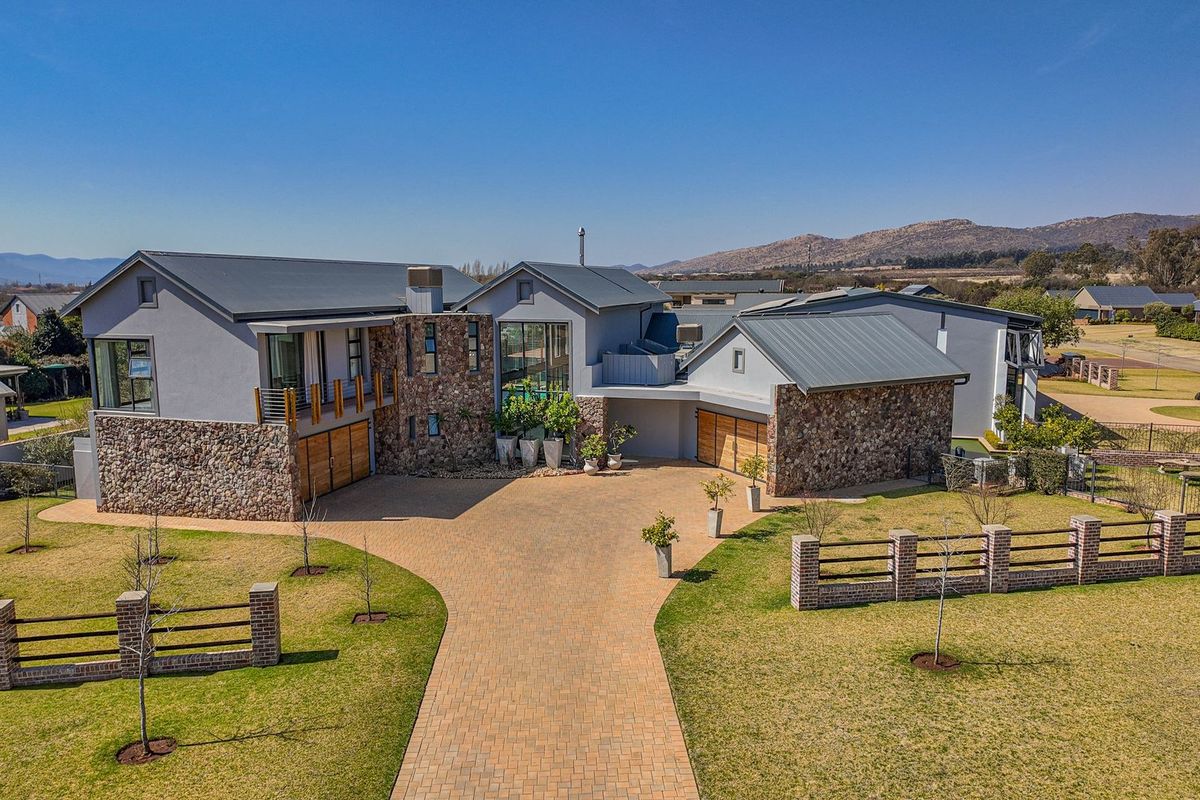 Aerial view of a modern luxury residence featuring stone cladding, metal roofing, a spacious paved driveway, and a well-maintained landscaped garden.