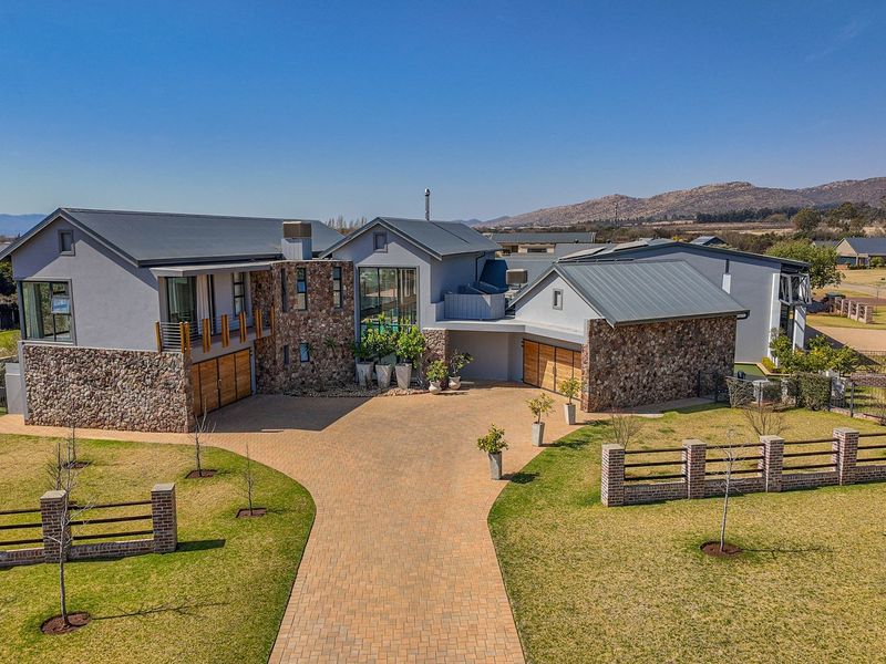 Aerial view of a modern luxury residence featuring stone cladding, metal roofing, a spacious paved driveway, and a well-maintained landscaped garden.