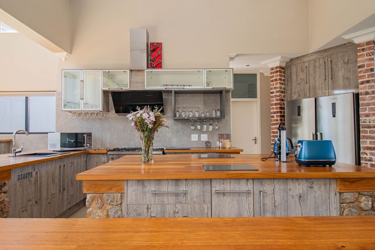 A spacious kitchen featuring rustic wooden countertops, a stone-clad island, exposed brick accents, and modern cabinetry with integrated appliances.