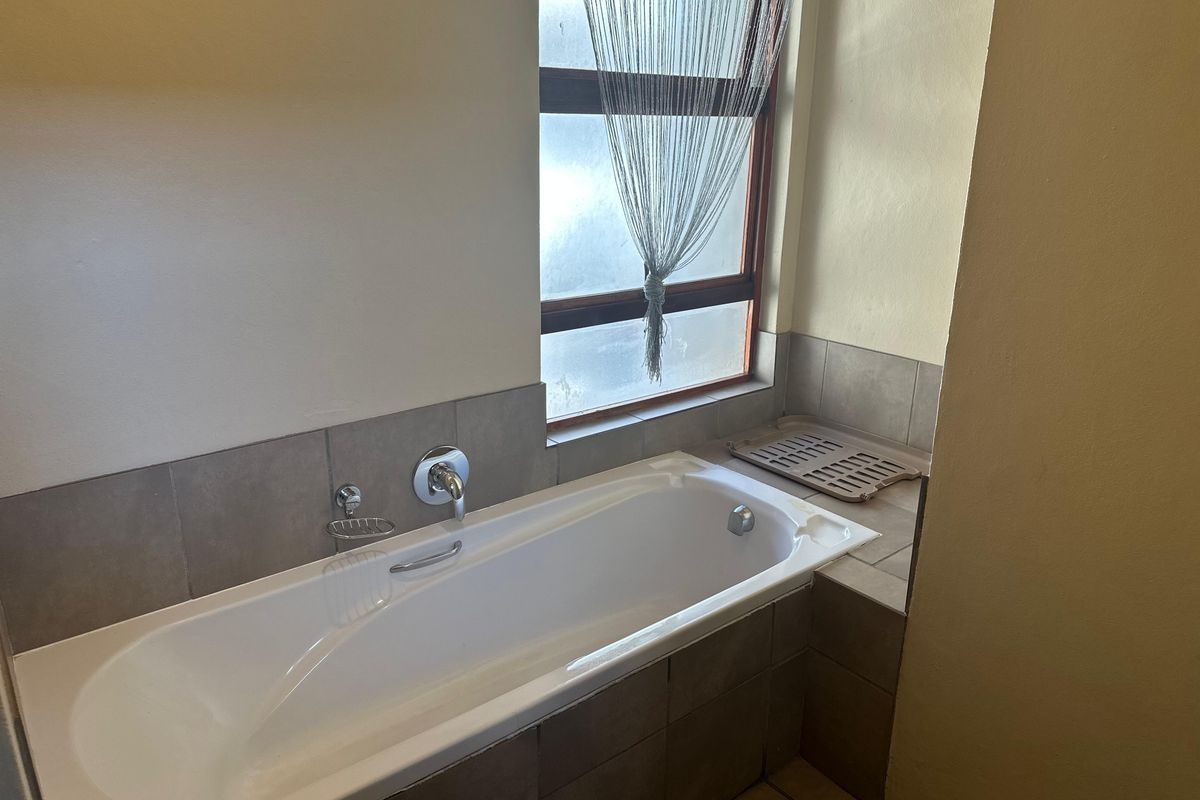 A functional bathroom featuring a built-in bathtub with tiled surround, chrome fixtures, and a frosted glass window for natural light.