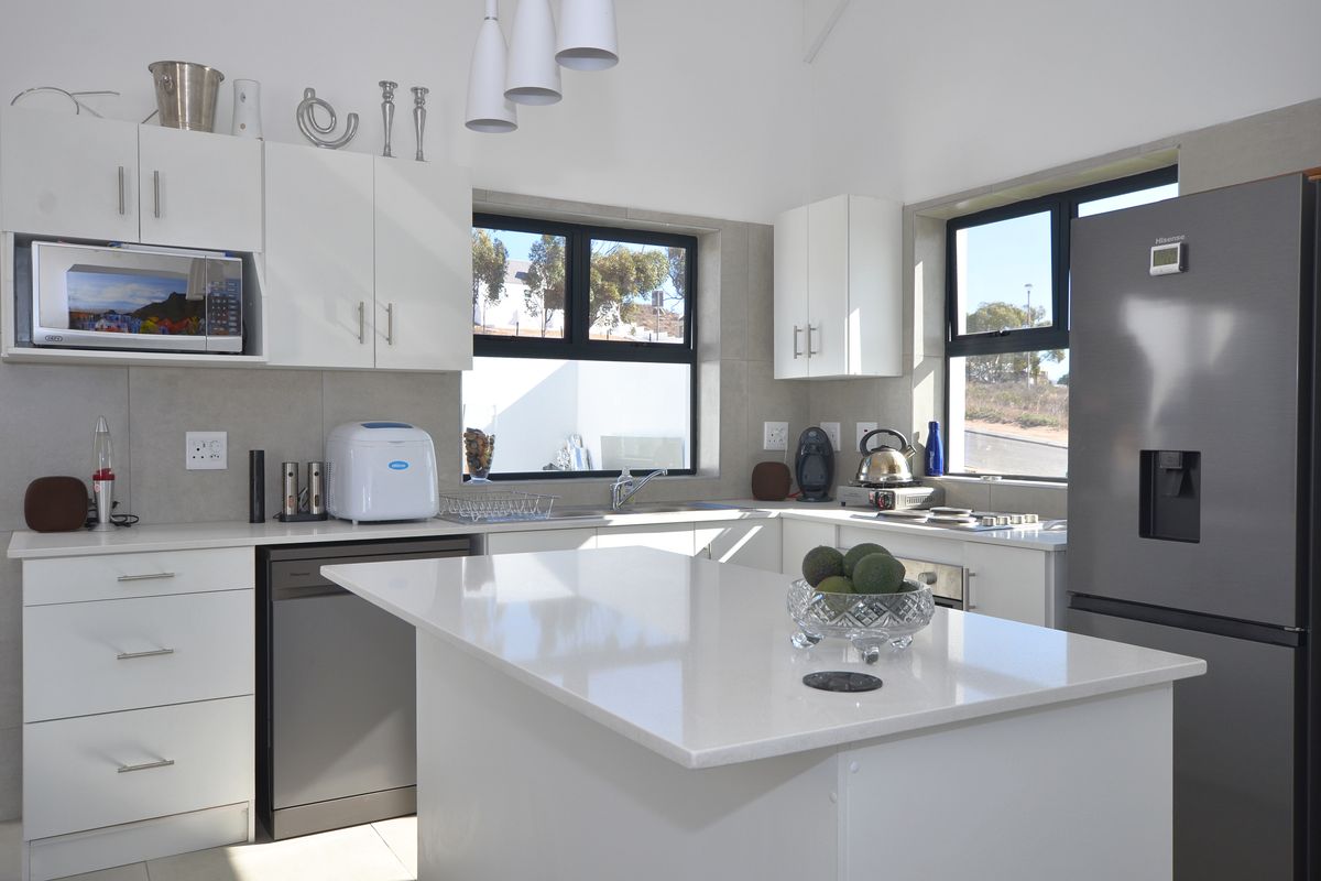 Modern kitchen featuring white cabinetry, stone countertops, a central island, and integrated stainless steel appliances, offering a clean and functional culinary space.