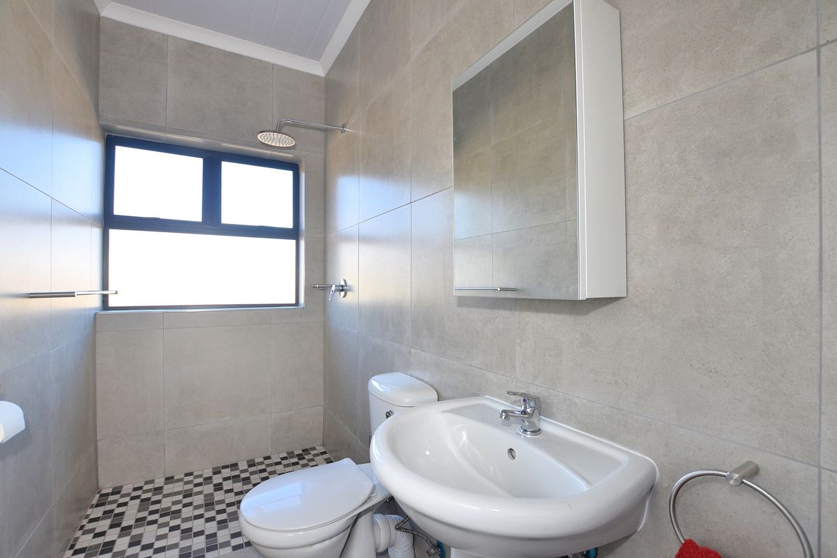 A modern bathroom featuring neutral wall tiling, a pedestal basin, a wall-mounted mirrored cabinet, a toilet, and a shower area with a mosaic floor.