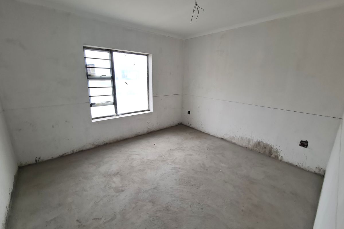 An unfinished bedroom space featuring raw plaster walls, exposed concrete flooring, and a steel-framed window, ready for final flooring and wall finishes.