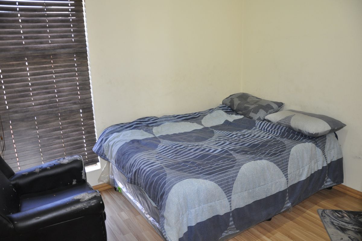 A bedroom featuring laminate flooring and dark wooden venetian blinds, providing a functional space for rest.