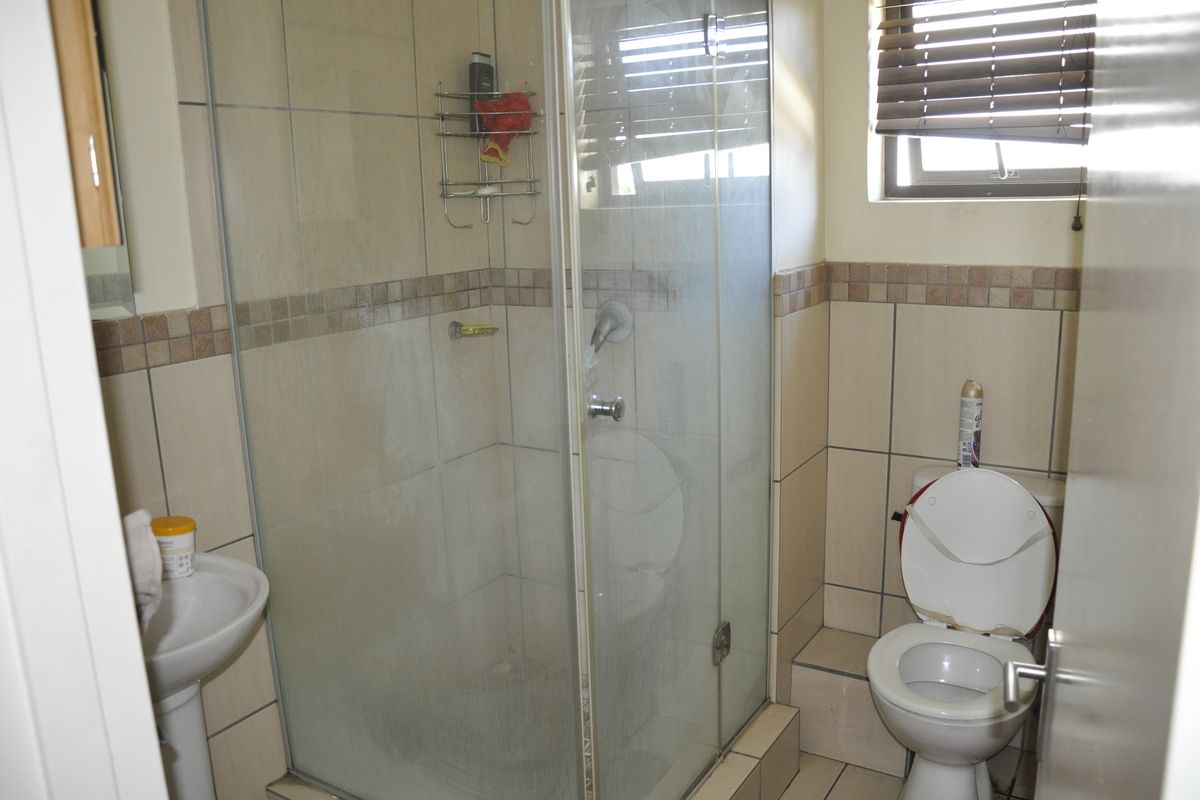 A functional bathroom featuring a glass-enclosed shower, pedestal basin, and toilet, finished with neutral wall and floor tiling.