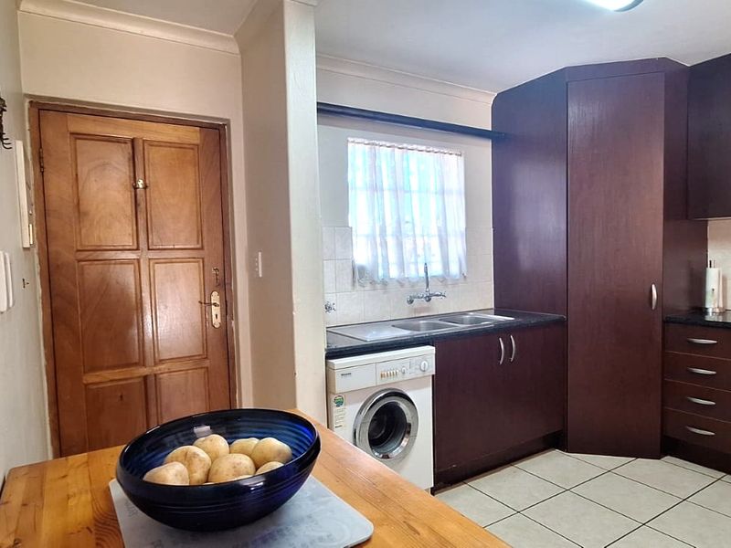Functional kitchen featuring dark wood cabinetry, built-in oven, electric hob, extractor fan, and integrated laundry plumbing.