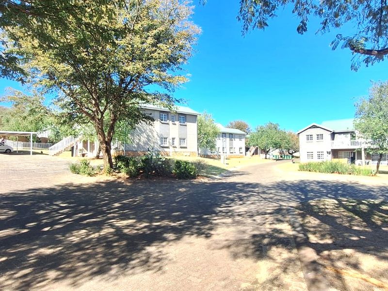 A view of the townhouse complex grounds featuring paved driveways, established trees, and covered parking areas for residents.
