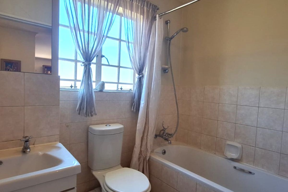 A functional bathroom featuring a bathtub with shower mixer, a built-in vanity with mirror, and neutral wall tiling.
