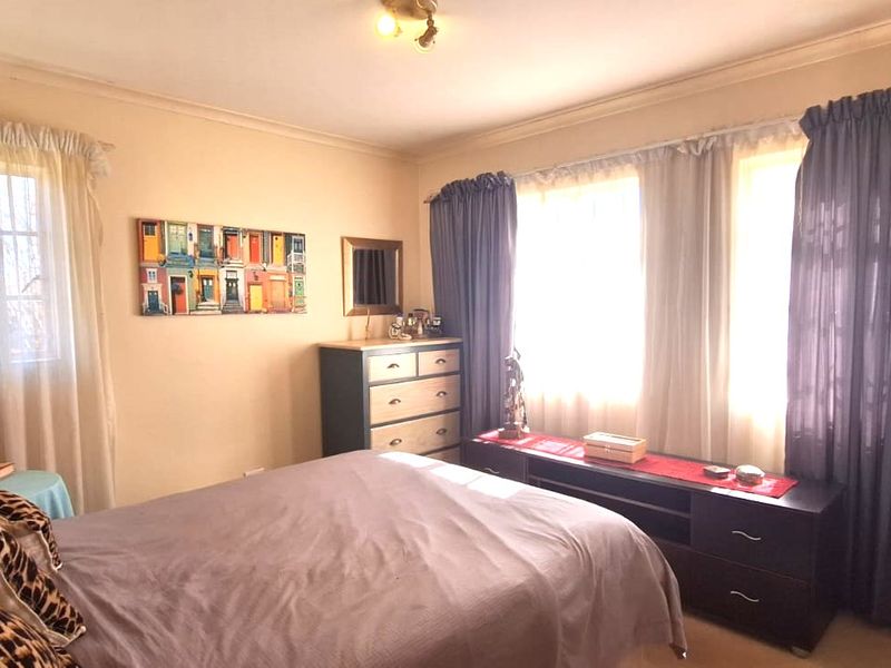 A standard bedroom featuring built-in cupboards, security bars on the windows, and neutral wall finishes.