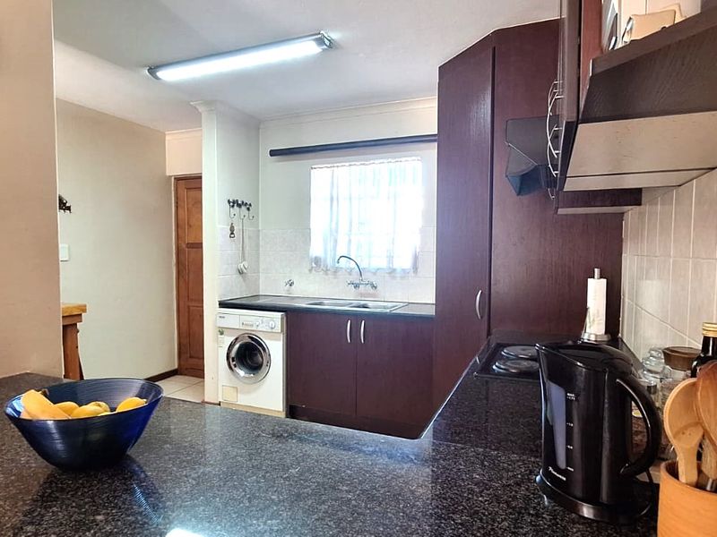 A functional kitchen featuring dark wood cabinetry, granite countertops, a built-in hob with extractor fan, and a dedicated space for a washing machine.