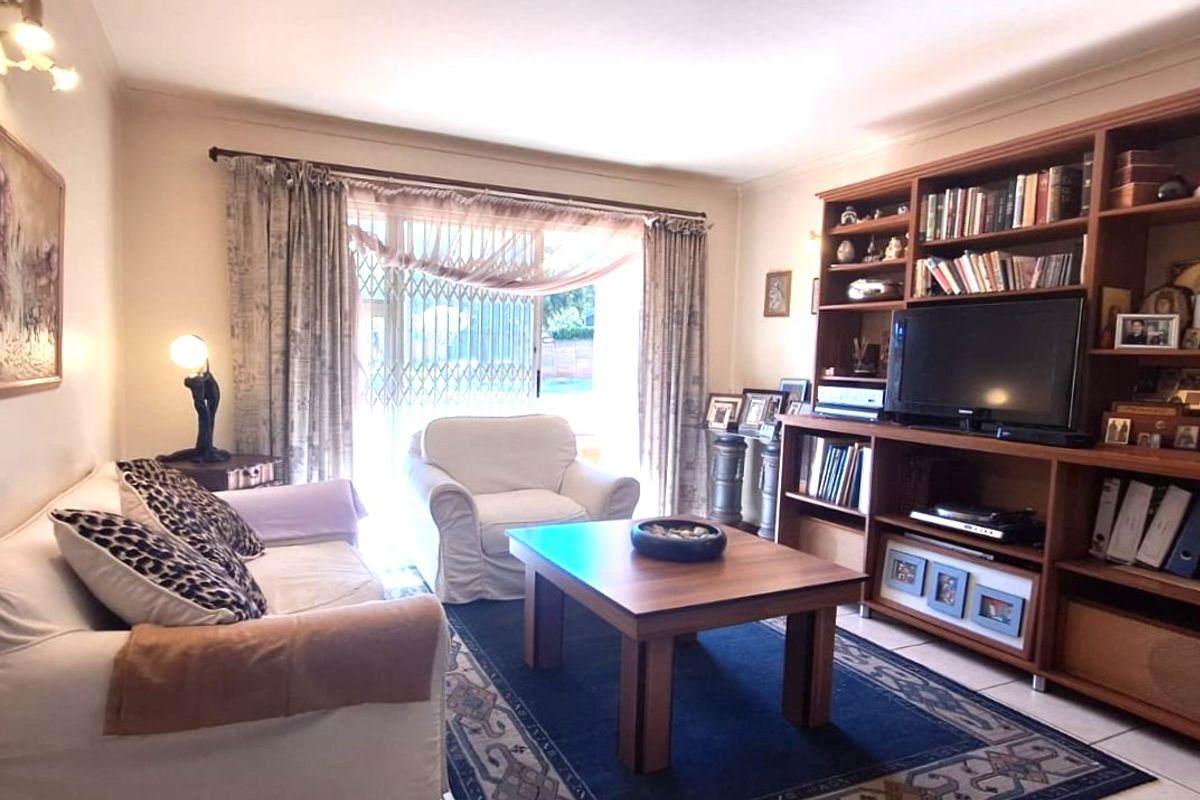 A comfortable living room featuring tiled flooring, a large built-in wooden shelving unit, and a sliding glass door with security gate access.