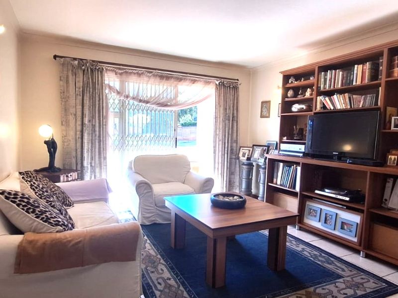 A comfortable living room featuring tiled flooring, a large built-in wooden shelving unit, and a sliding glass door with security gate access.