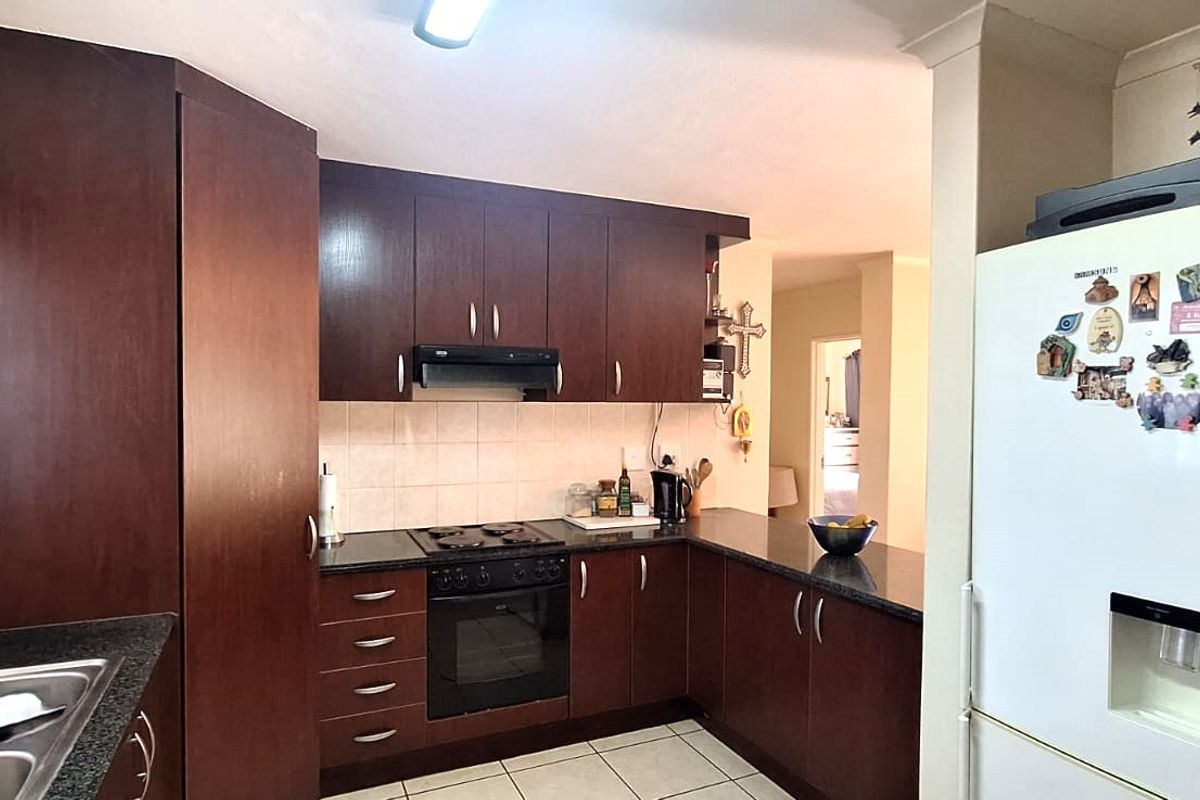 Functional kitchen featuring dark wood cabinetry, granite countertops, built-in oven, hob, extractor fan, and tiled flooring with a practical layout.