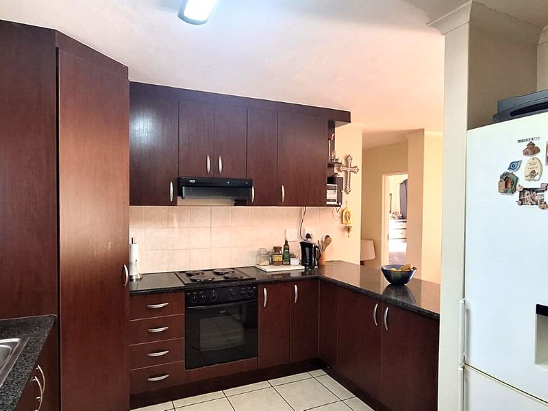 Functional kitchen featuring dark wood cabinetry, granite countertops, built-in oven, hob, extractor fan, and tiled flooring with a practical layout.