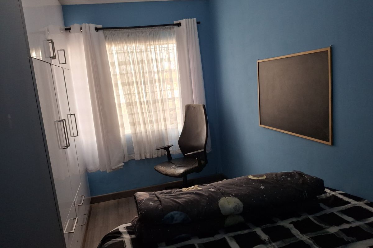 A bedroom featuring built-in white cabinetry, laminate flooring, and a window with security bars, providing a functional and compact living space.