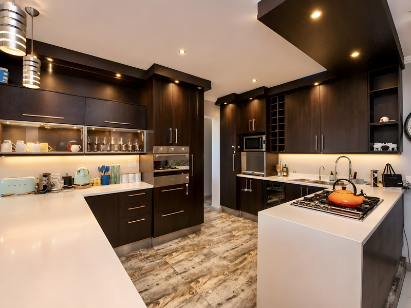 Modern kitchen featuring dark wood cabinetry, sleek quartz countertops, integrated appliances, and sophisticated under-cabinet and pendant lighting for a contemporary finish.