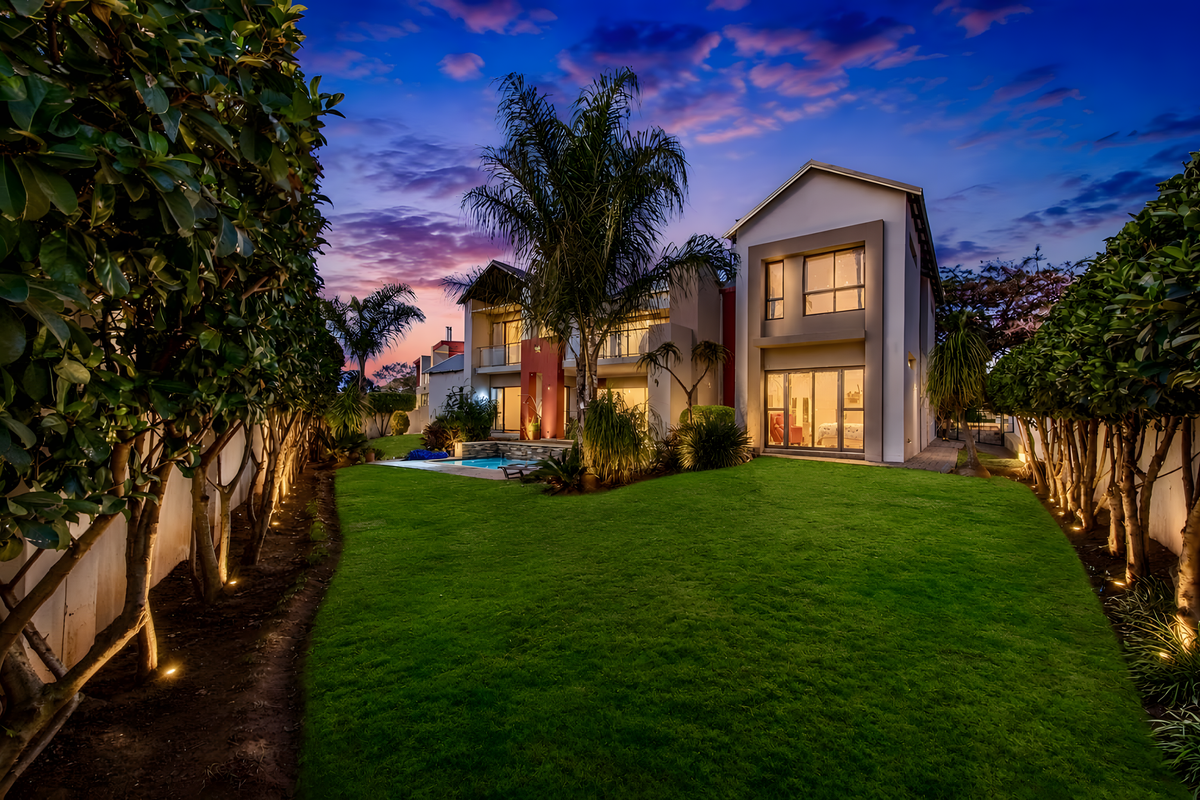 A beautifully landscaped rear garden featuring a swimming pool, manicured lawn, and exterior lighting, set against the modern rear facade of the house.