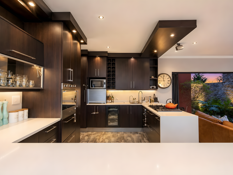 Modern kitchen featuring dark wood cabinetry, stone countertops, integrated appliances, and recessed lighting, seamlessly flowing into an outdoor living area.