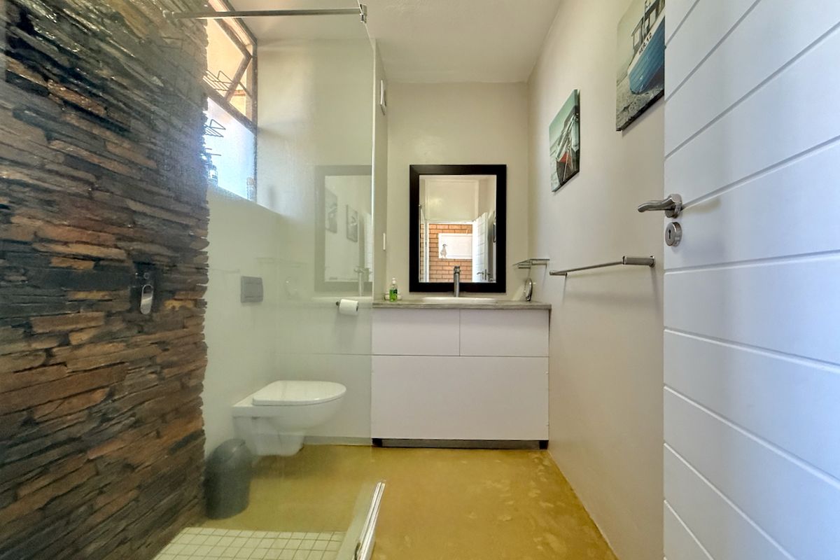 Modern bathroom featuring a stone accent wall, glass-enclosed shower, wall-mounted toilet, and a clean white vanity cabinet.