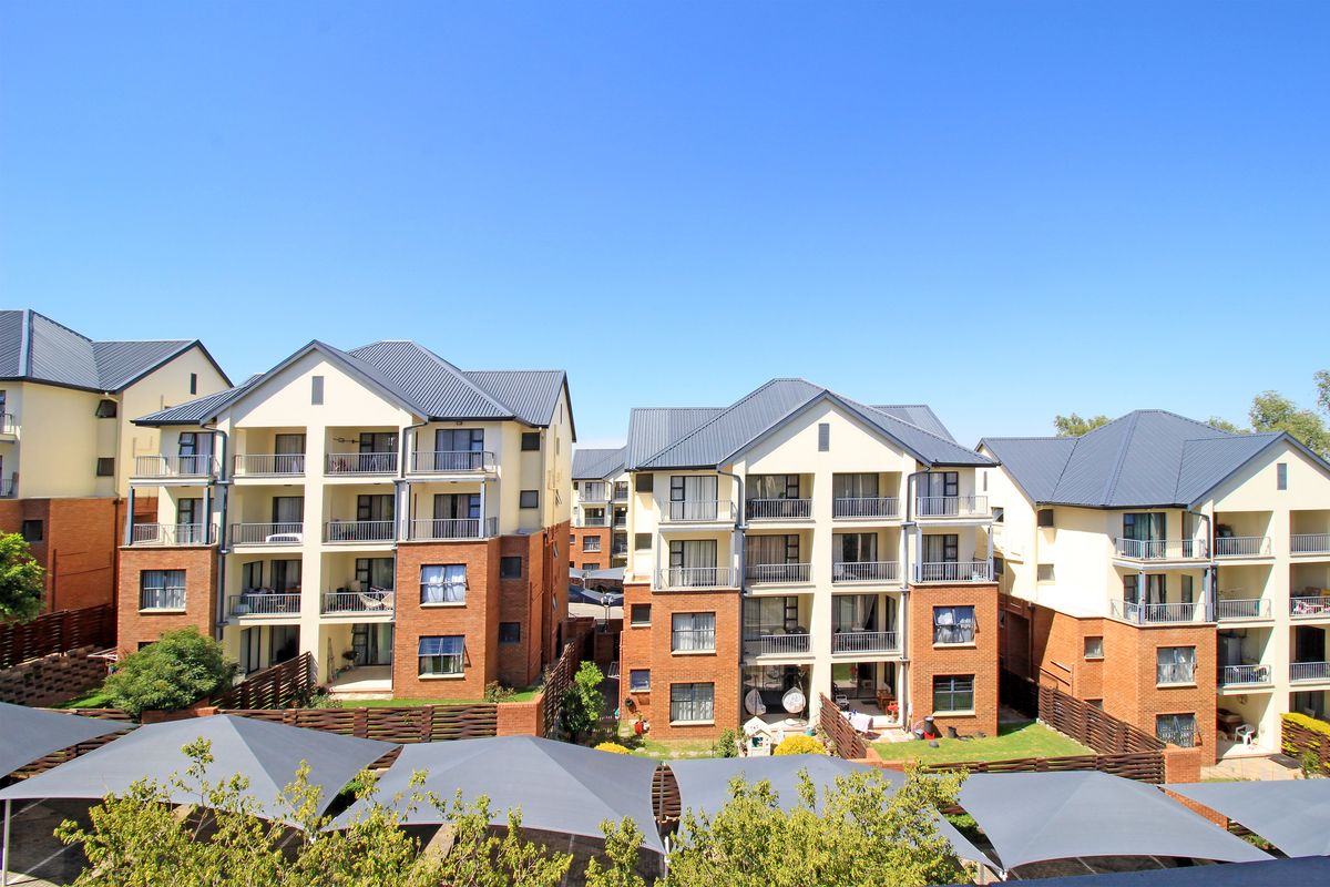 A view of the rear elevation of a multi-story apartment complex featuring brick and plaster facades, metal roofing, and private balconies.