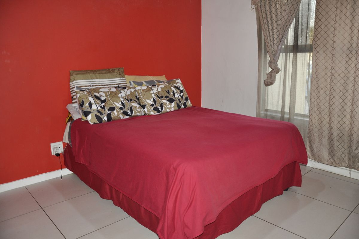 A bedroom featuring tiled flooring and a bold red accent wall, providing a functional space with natural light from the window.
