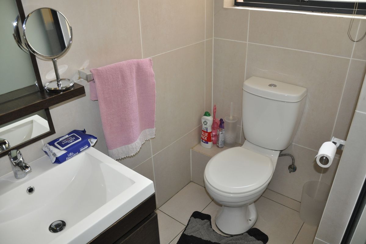 A compact bathroom featuring neutral ceramic wall and floor tiles, a modern vanity basin, and a standard toilet.