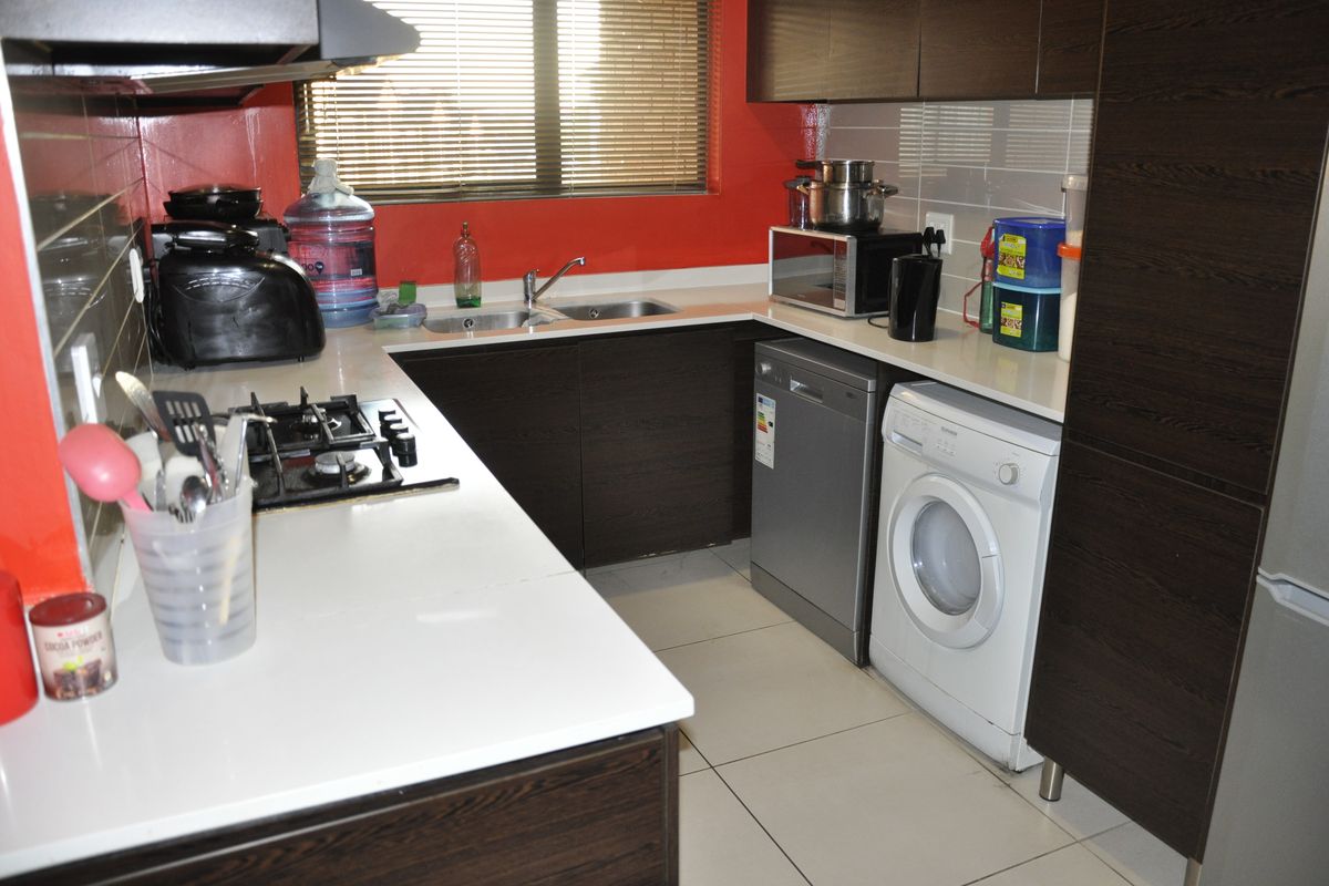 A functional kitchen featuring dark wood cabinetry, stone countertops, a gas hob with extractor, and integrated space for laundry and dishwashing appliances.