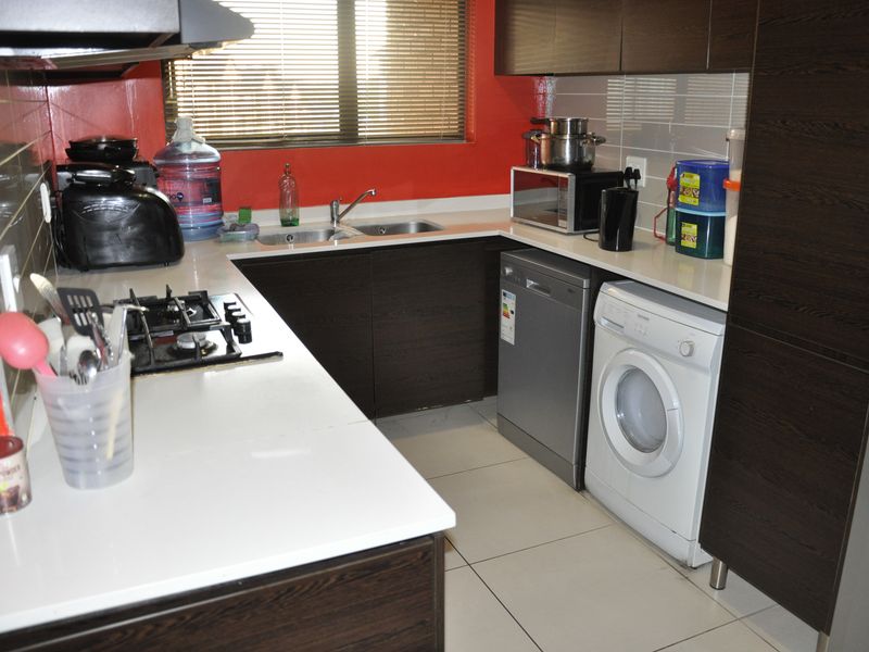A functional kitchen featuring dark wood cabinetry, stone countertops, a gas hob with extractor, and integrated space for laundry and dishwashing appliances.