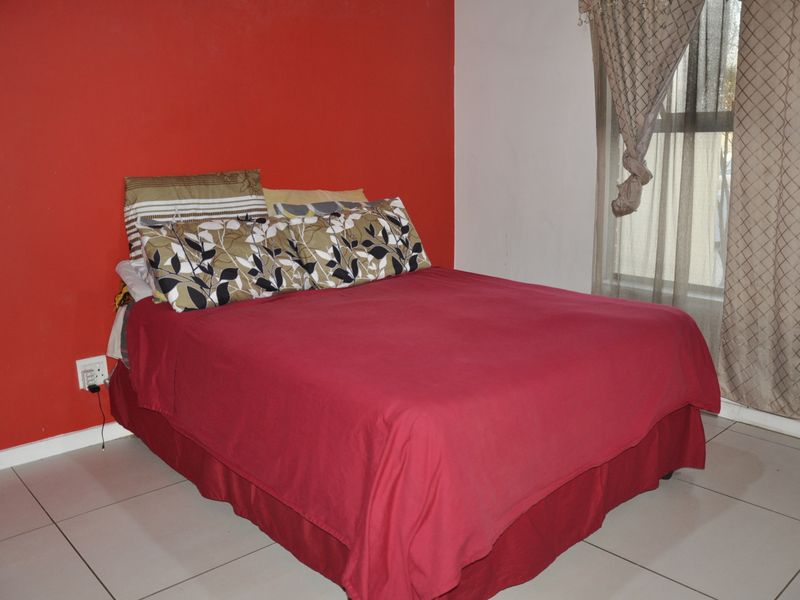 A bedroom featuring tiled flooring and a bold red accent wall, providing a functional space with natural light from the window.