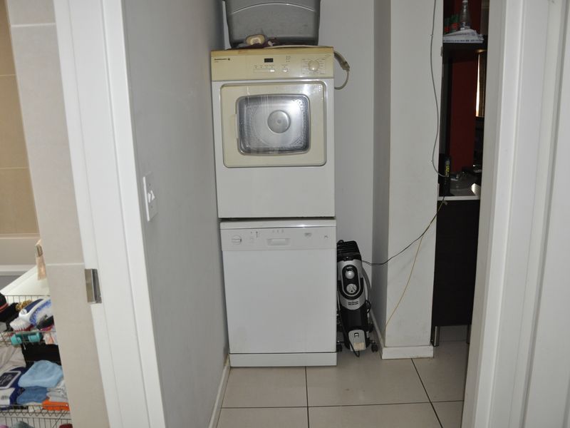A compact laundry nook featuring tiled flooring and space for stacked laundry appliances.