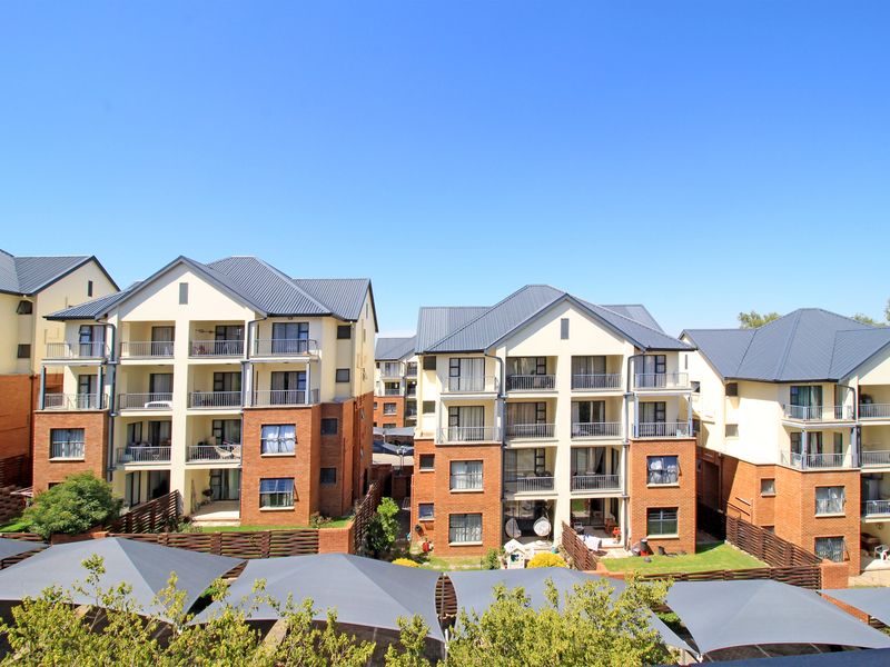A view of the rear elevation of a multi-story apartment complex featuring brick and plaster facades, metal roofing, and private balconies.