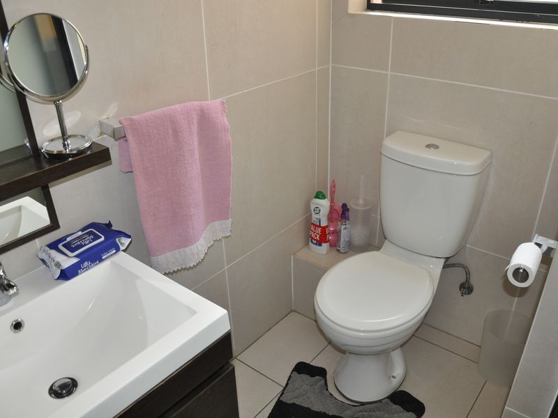 A compact bathroom featuring neutral ceramic wall and floor tiles, a modern vanity basin, and a standard toilet.