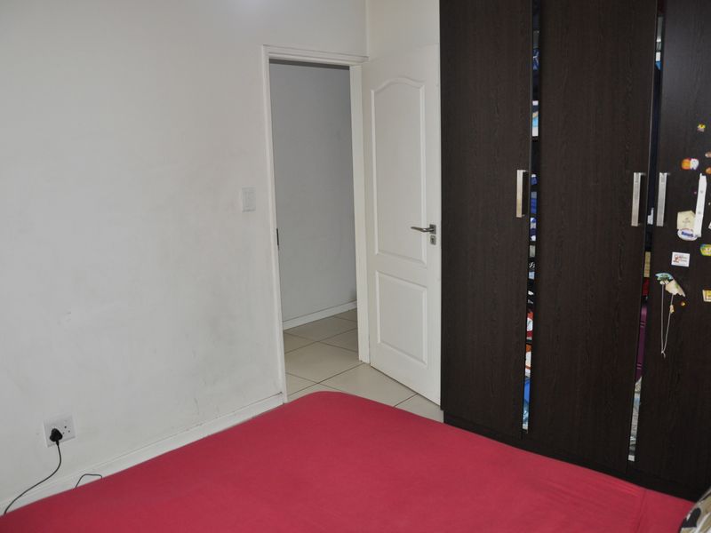 A bedroom featuring tiled flooring and a dark wood built-in wardrobe, with an internal door leading to an adjacent space.