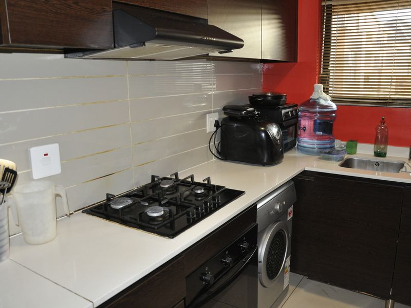 Compact kitchen featuring dark wood-finish cabinetry, a gas hob with extractor fan, built-in oven, and a stainless steel sink with tiled backsplash.