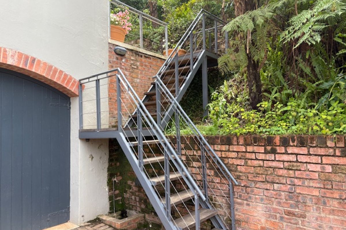 Exterior view featuring a metal staircase with cable railings leading up a brick retaining wall, adjacent to a garage entrance.