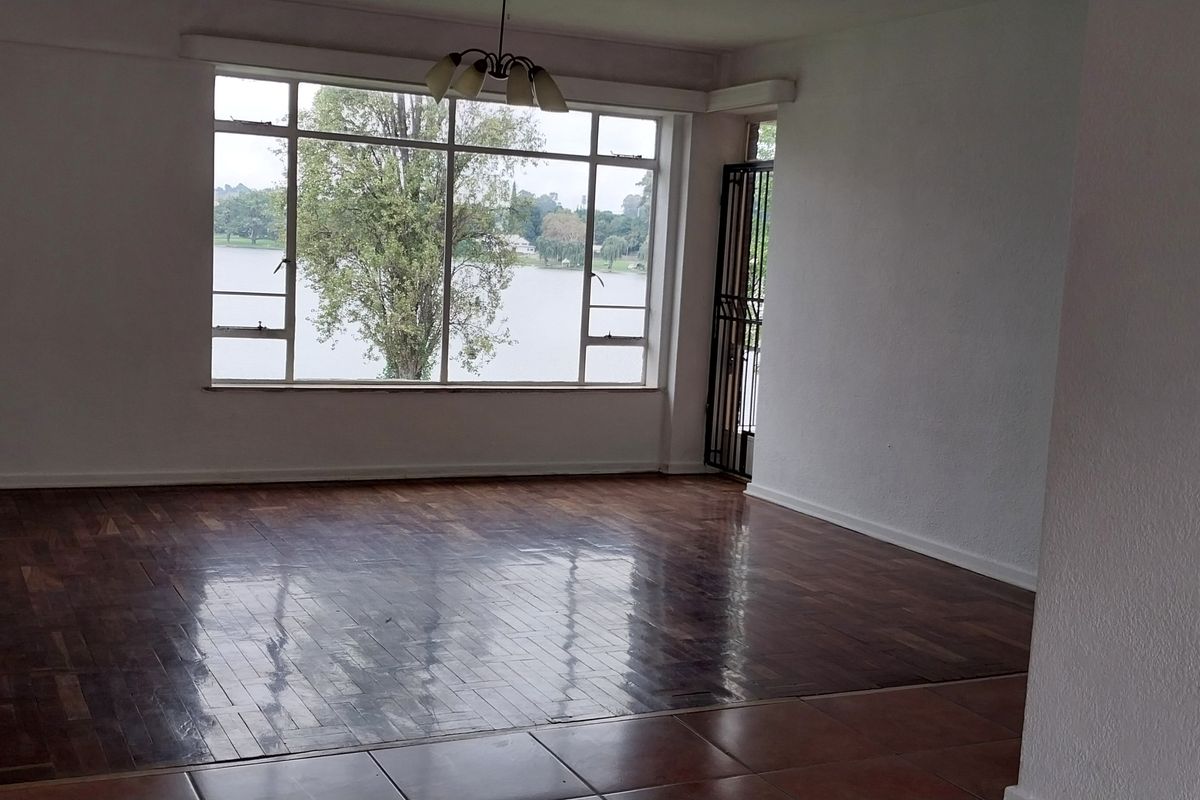 Spacious, empty living room featuring polished parquet flooring, large windows with scenic water views, and a secure entrance gate.